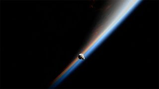 The SpaceX-25 Dragon cargo ship with a sliver of Earth illuminated by the sun in the background on July 16, 2022.