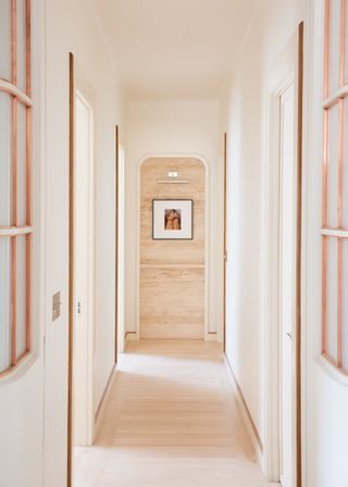 A hallway with white walls, copper trimmings and wooden floors.