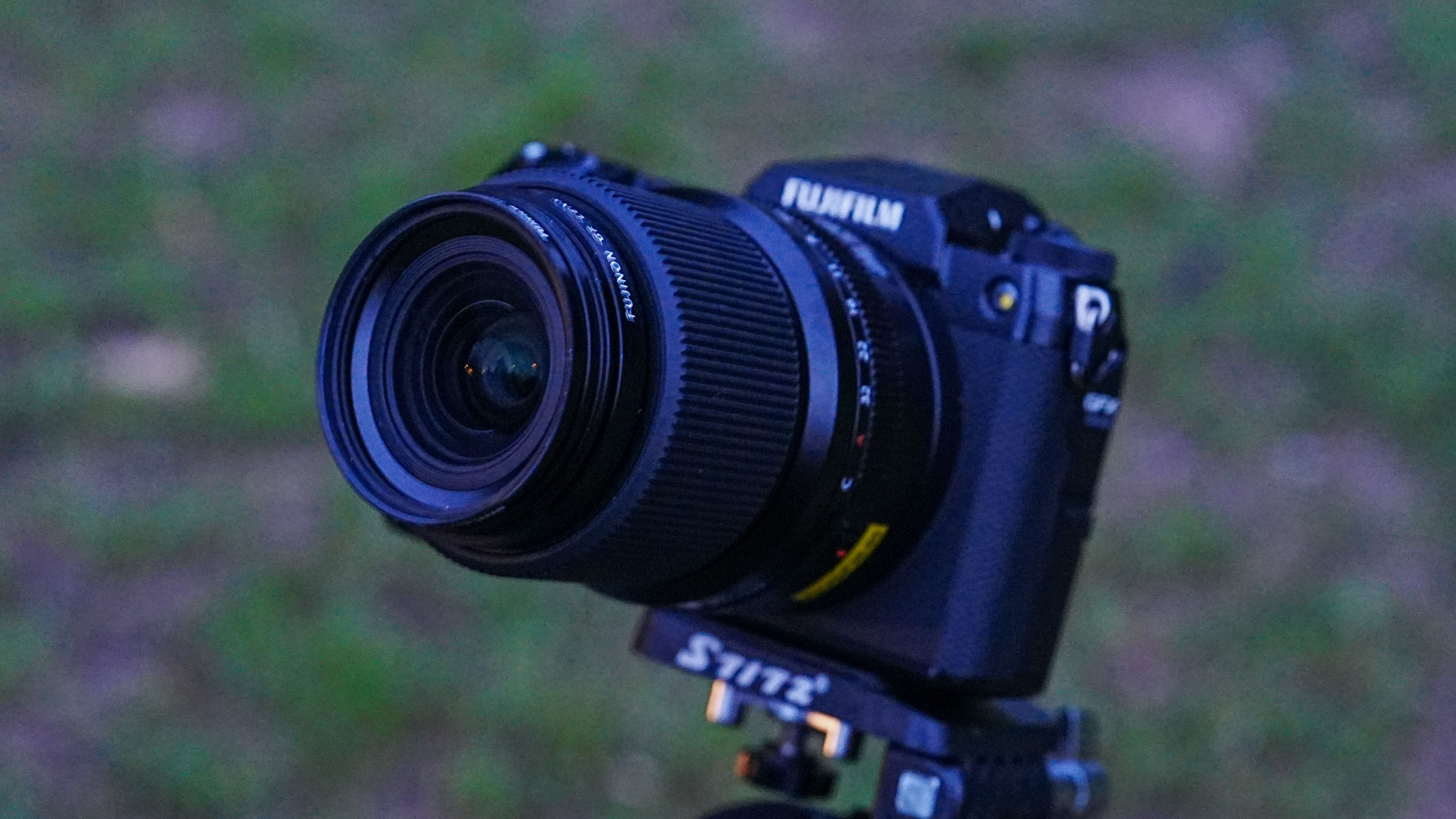 The Fujifilm GFX100S II with the Fujifilm GF 30mm f/3.5 R WR lens attached on a tripod with grass in the background.