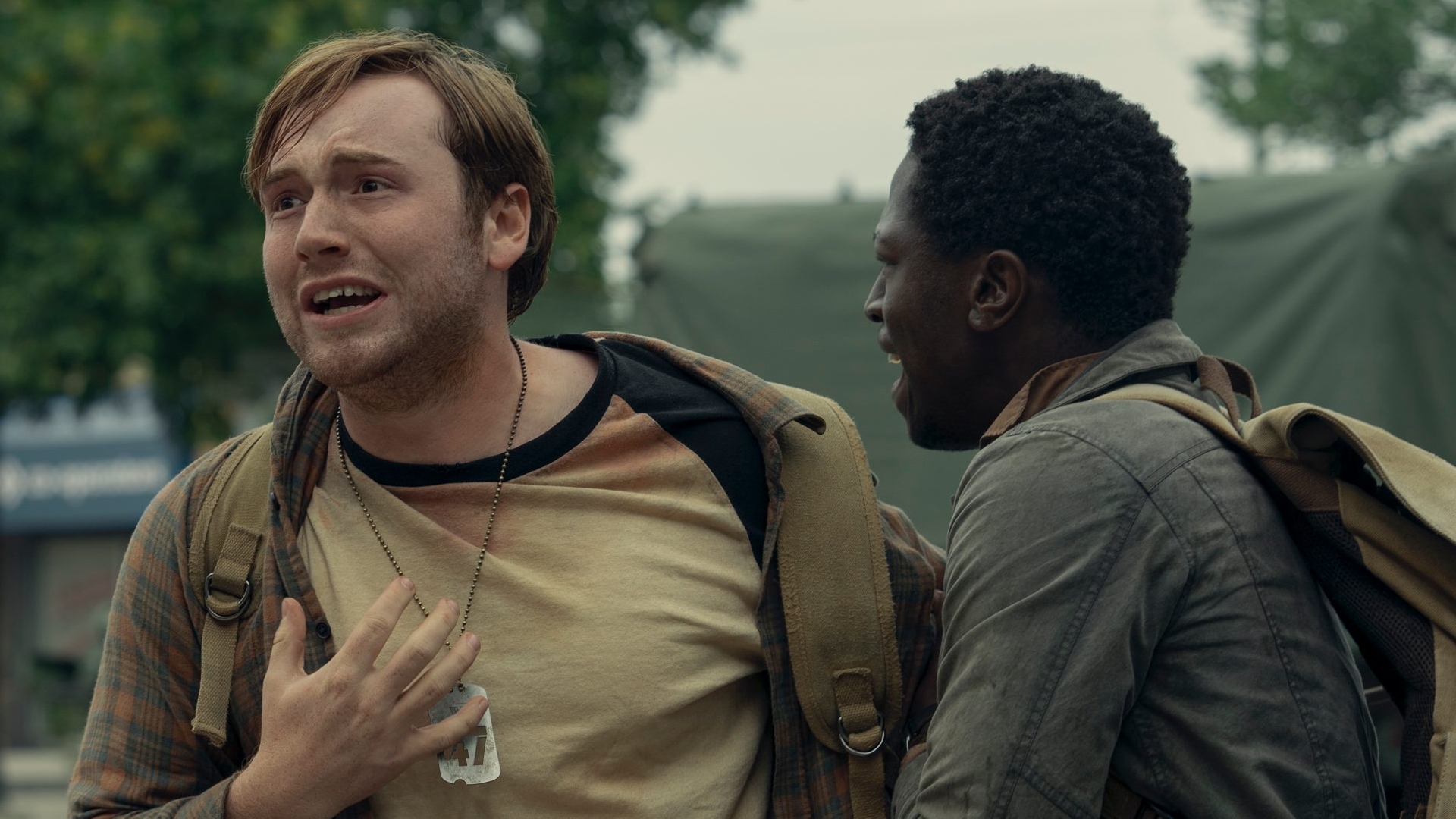 Two men wear dog tags and look panicked in The Long Walk