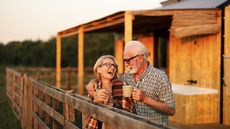 An older couple drink coffee and laugh together at sunrise at a cabin.