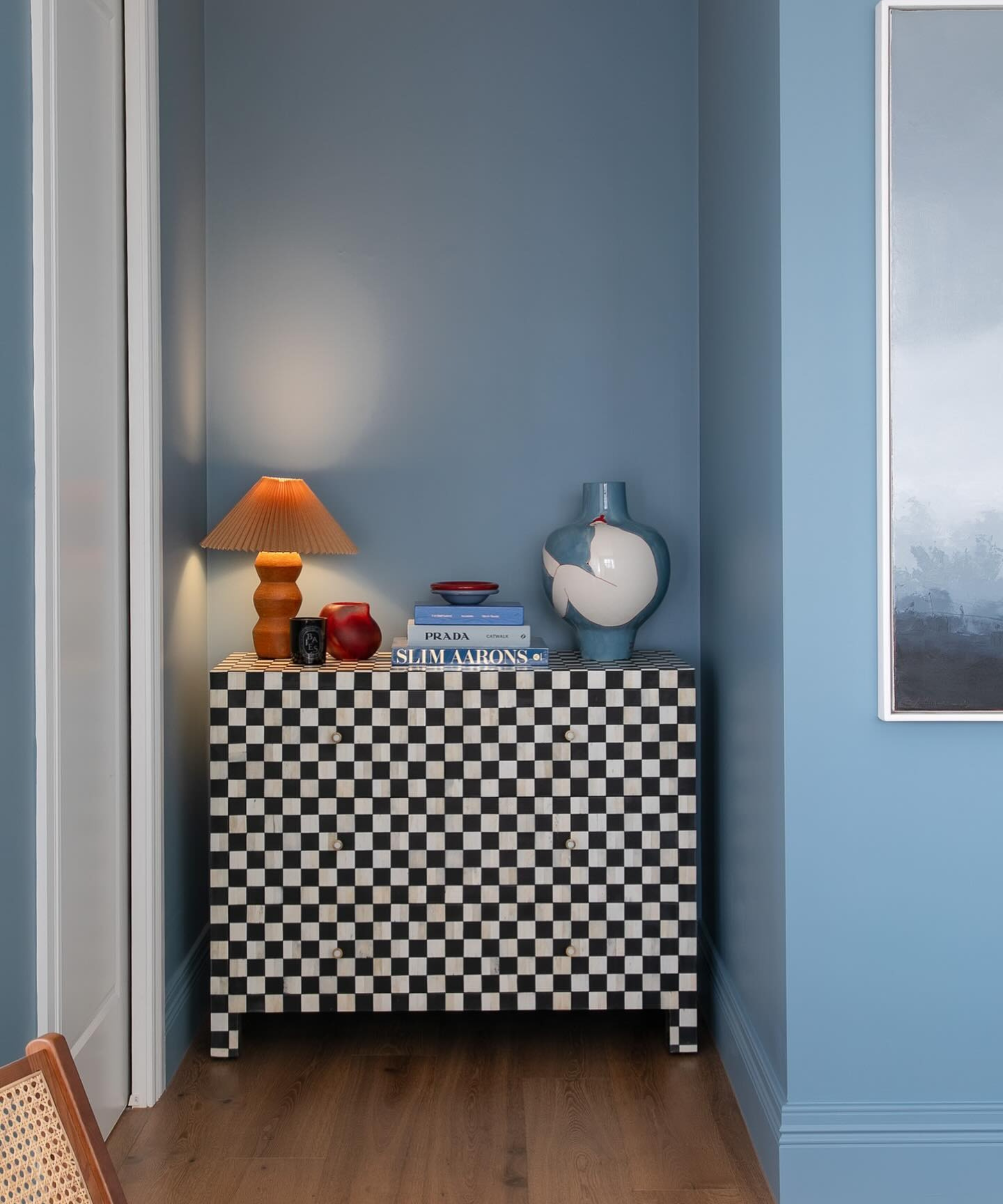 a nook in a blue painted room with a checkerboard dresser with decor on top