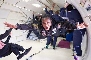 People floating in an airplane during a parabolic flight. At the front, a person stretches out their hands while smiling.