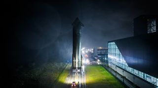 a large silver rocket rolls vertically down a road at night