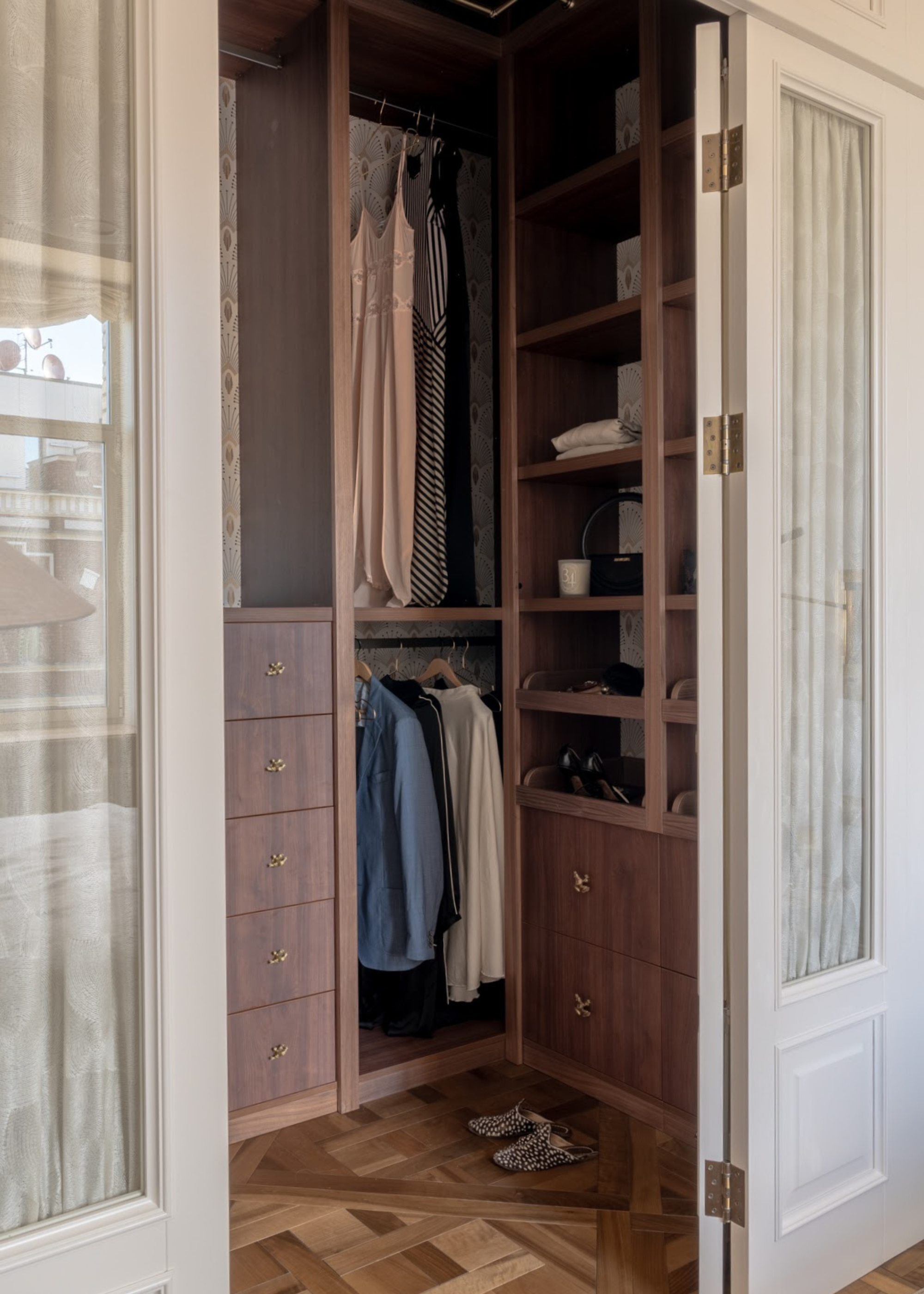 A white wardrobe with wooden shelves, rows of clothes on hangers, and a pair of shoes on wood floors