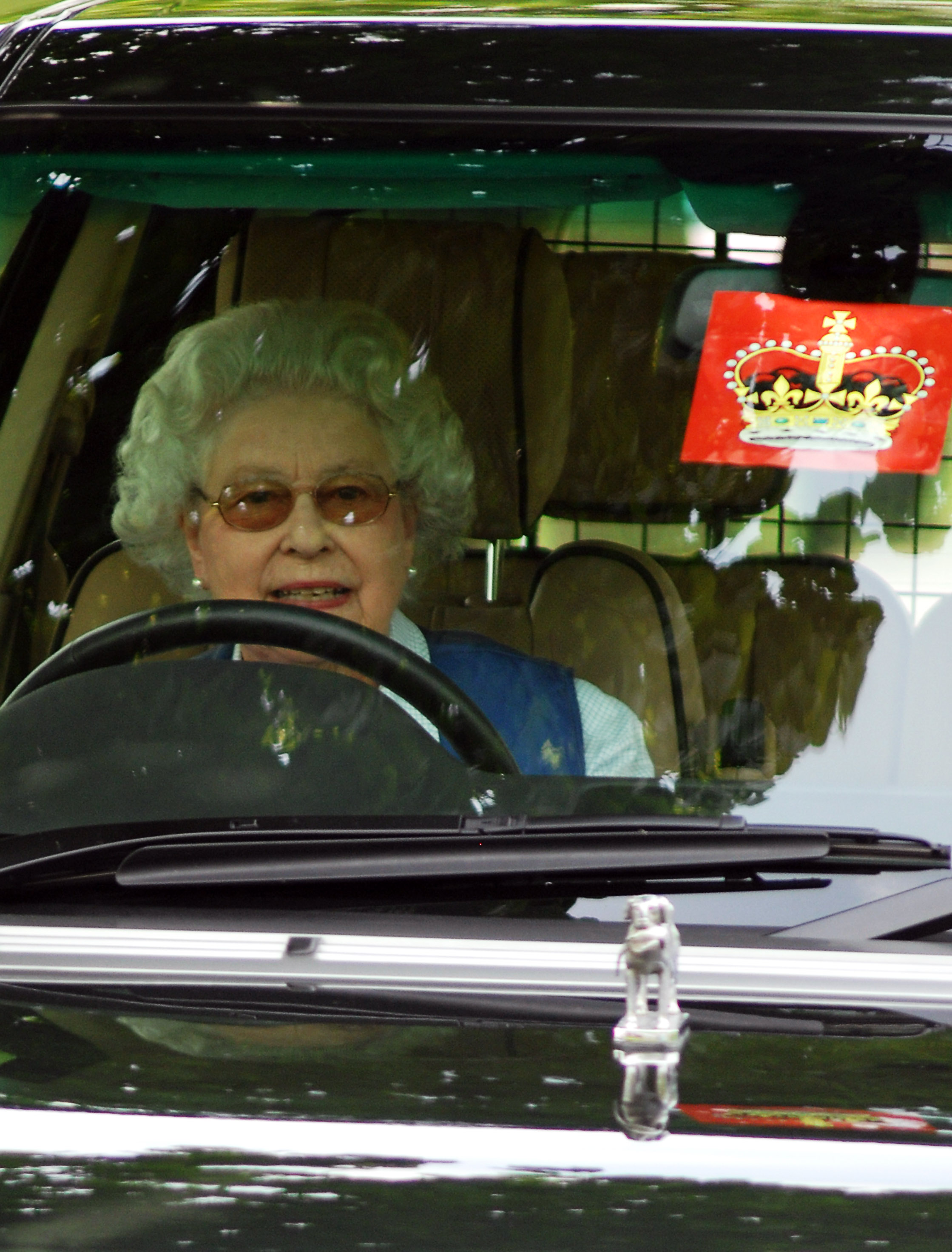 Queen Elizabeth driving a Range Rover with a red crown sticker on the window