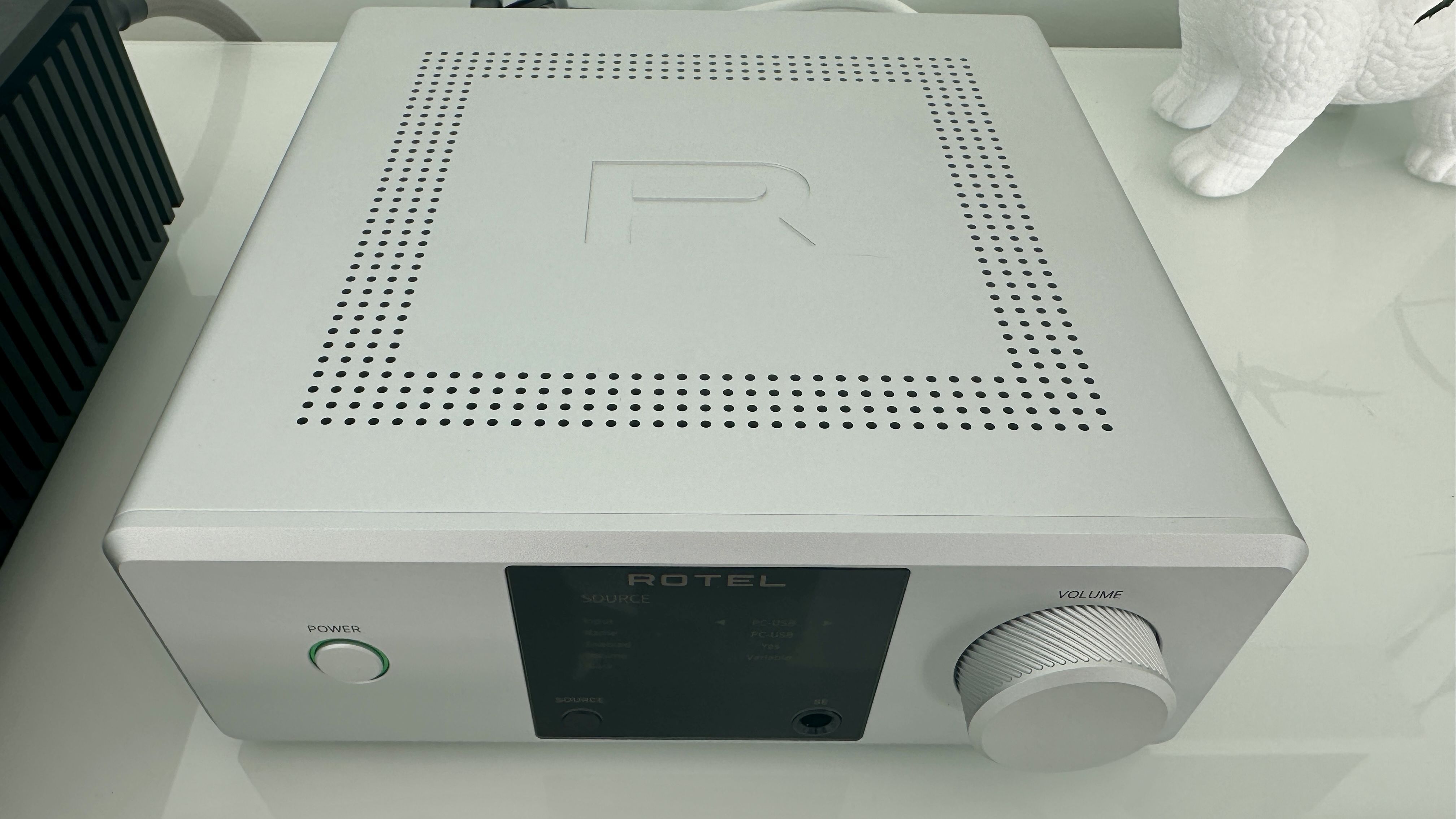 Rotel's DX-5 integrated amp in silver on a light gray table, with the amp's remote visible