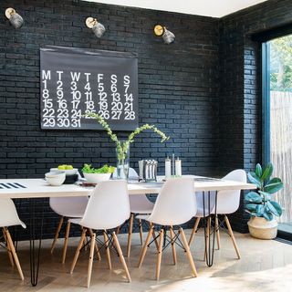 Dining space with white table and chairs and black painted exposed brick wall