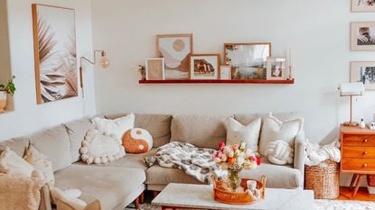 A small living room with a gray L-shaped couch, shelves, and a coffee table with decor on
