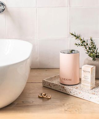 A pink NEOM mini diffuser on a stonewear tray in a bathroolm