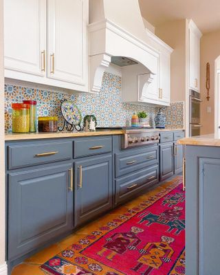 Kitchen with cool blue cabinets and brightly colored mosaic tiled backsplash with rug.
