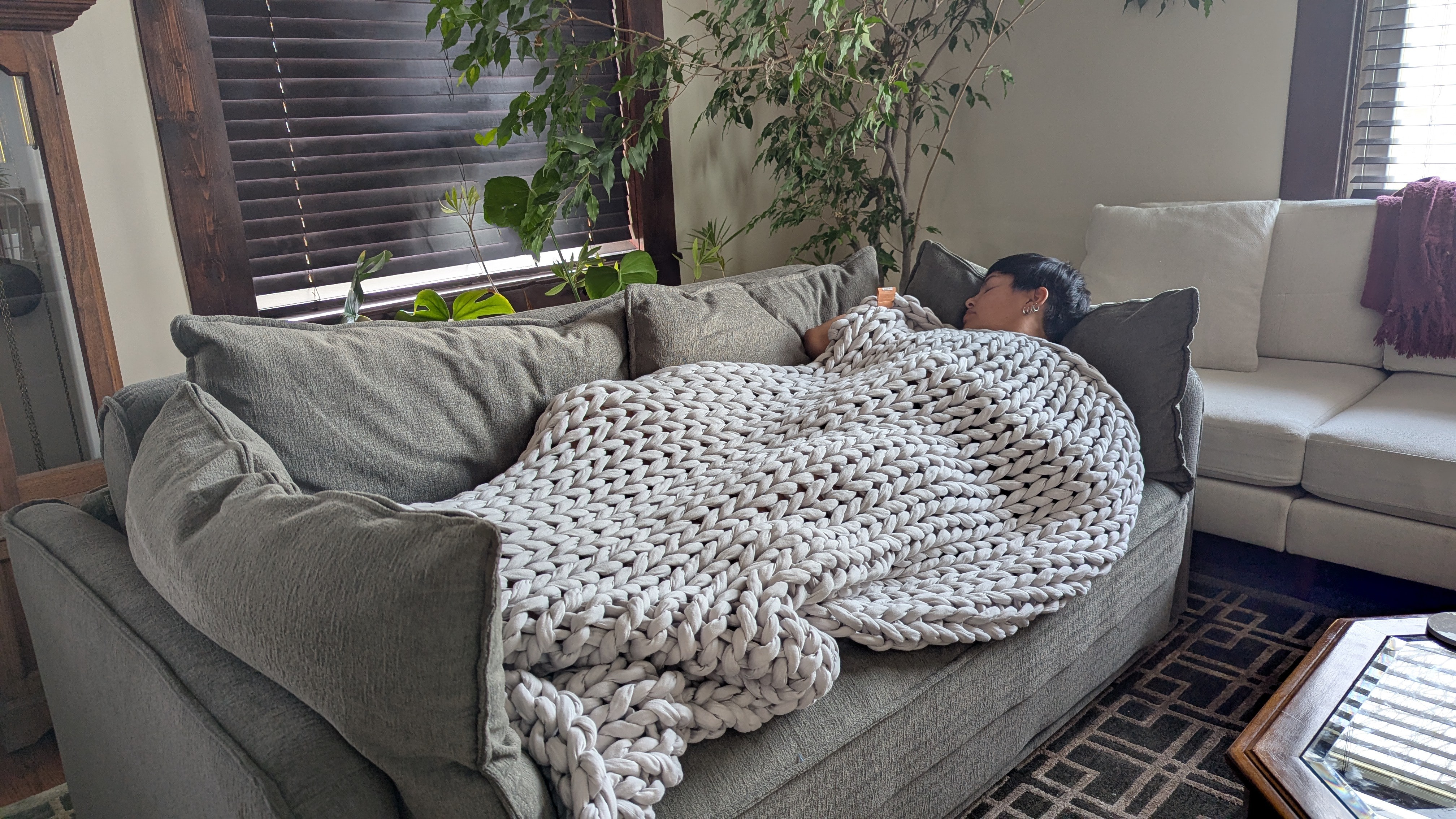 Woman sleeping on a grey sofa with a grey knitted weighted blanket draped on top