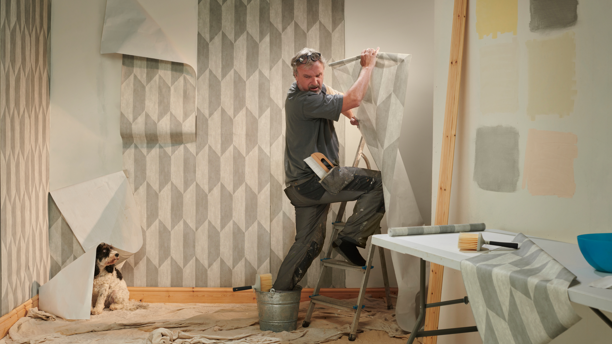 man wallpapering room with foot stuck in bucket and wallpaper hanging off walls