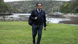 Sunny in Ireland walking along the shoreline, wearing a dark jacket and a backpack.