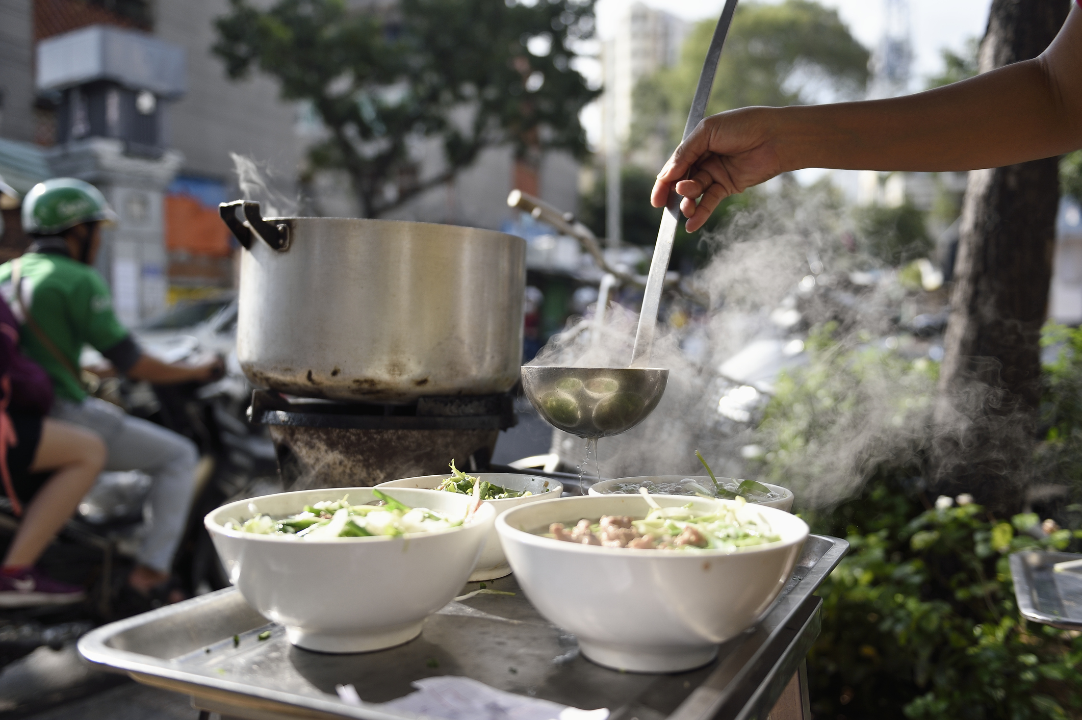 Hands pouring broth into bowls of pho.