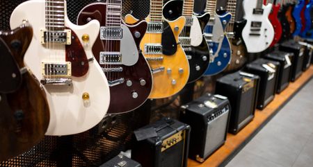 A rack of Gretsch guitars in a guitar store, with a line of budget amps on the floor.