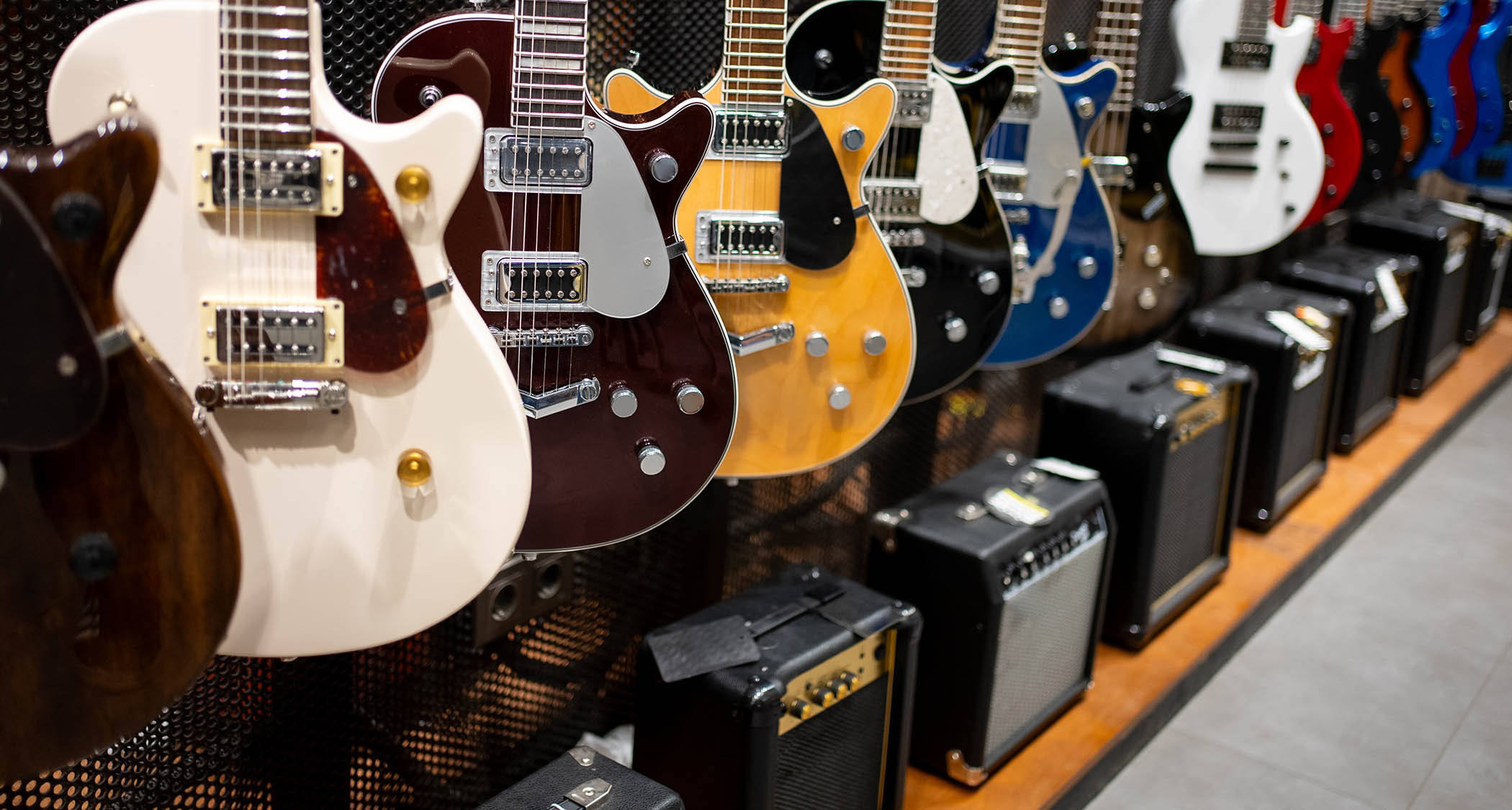A rack of Gretsch guitars in a guitar store, with a line of budget amps on the floor
