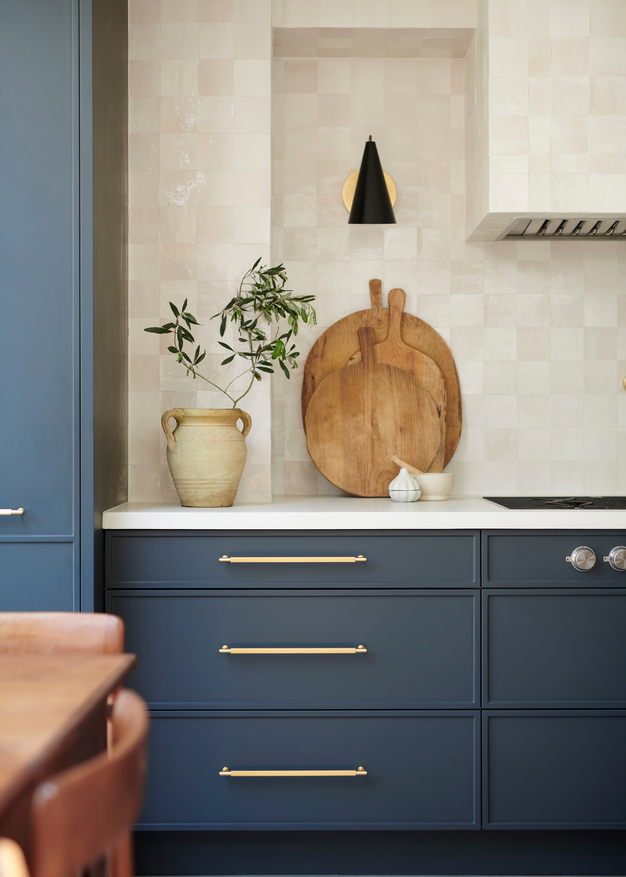 dark blue cabinet drawers with a creamy zellige tile back splash. on the counter is a vase with a plant inside as well as wooden chopping boards