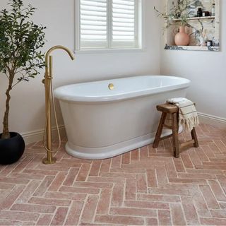 A bathroom with a freestanding bath and terracotta floor tiles