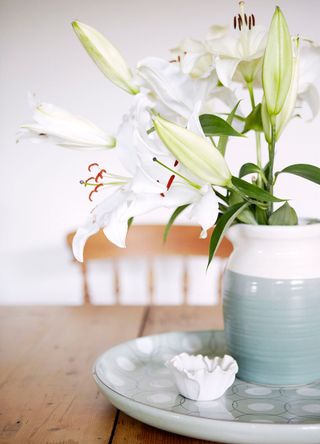 pot of white lilies on top of a wooden dining table