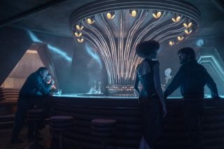 Cassian Andor talks to a hostess (Margaret Cline) while Kravas (Lee Boardman) and Verlo (Stephen Wright) look on, in Andor