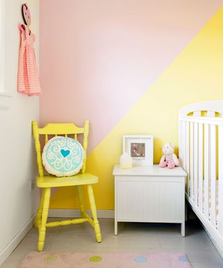 childrens room with wooden floor and multicolour wall with yellow chair with round cushion and white bedside table with bed rail