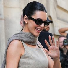 Kendall wears sunglasses, a gray scarf, and gray long dress.