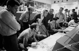 During the problematic Apollo 13 mission, six NASA astronauts and two flight controllers monitor console activity in the Mission Operations Control Room of the Mission Control Center (now known as the Johnson Space Center) in Houston. The Apollo 13 moon landing was canceled due to an explosion in the service module, and at the time of this image, the Apollo 13 crewmen were trying to make it back to Earth in the damaged spacecraft. Sitting at the console, from left to right: control room guidance officer Raymond Teague, Apollo 14 lunar module pilot Edgar Mitchell and Apollo 14 Cmdr. Alan Shepard. Standing behind them are, from left to right, NASA astronaut Anthony W. England, Apollo 14 backup crewmembers Joe Engle, Gene Cernan and Ron Evans, along with M.P. "Pete" Frank, a flight controller.