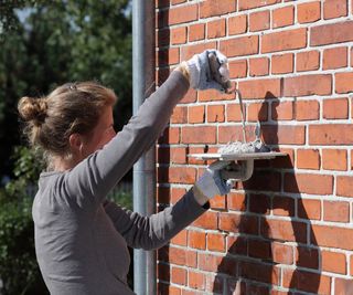 woman repointing brick wall