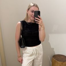 Woman wears black top, white linen trousers, carries black bag
