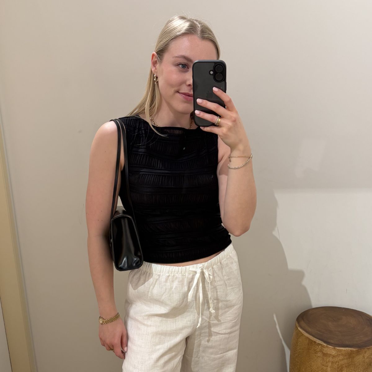 Woman wears black top, white linen trousers, carries black bag