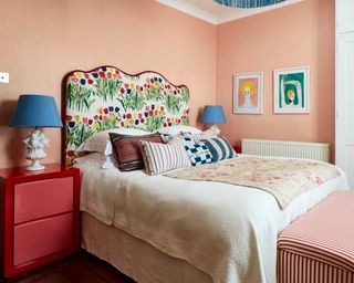 colorful bedroom with pink walls, patterned headboard, red beside chest and striped ottoman