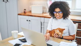 a smiling woman works on a computer with a cat on her lap