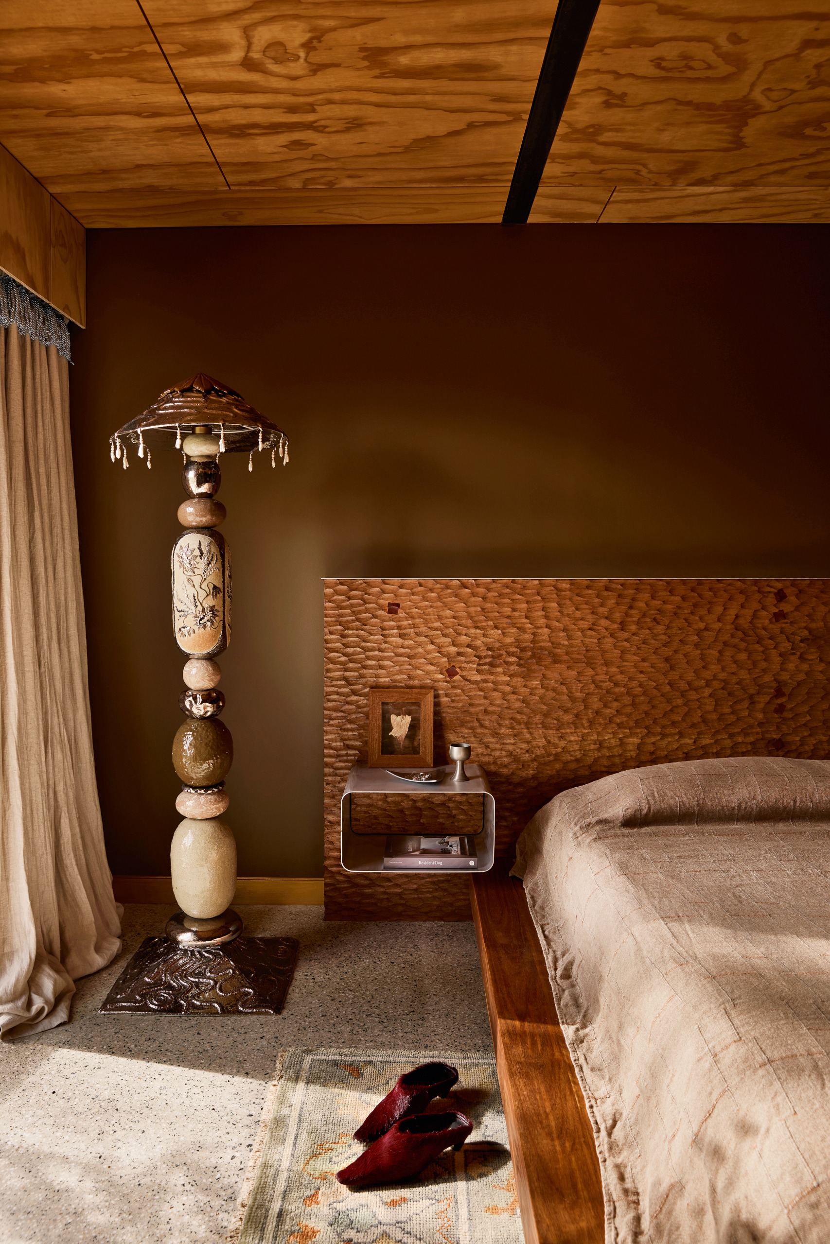 Dark brown bedroom with dimpled wood headboard, wood tiled ceiling and totem-style floor lamp