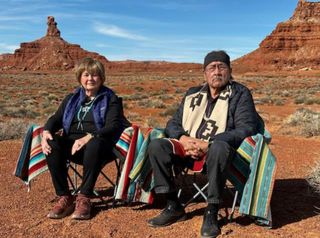 two people sit in chairs in the desert under a blue sky