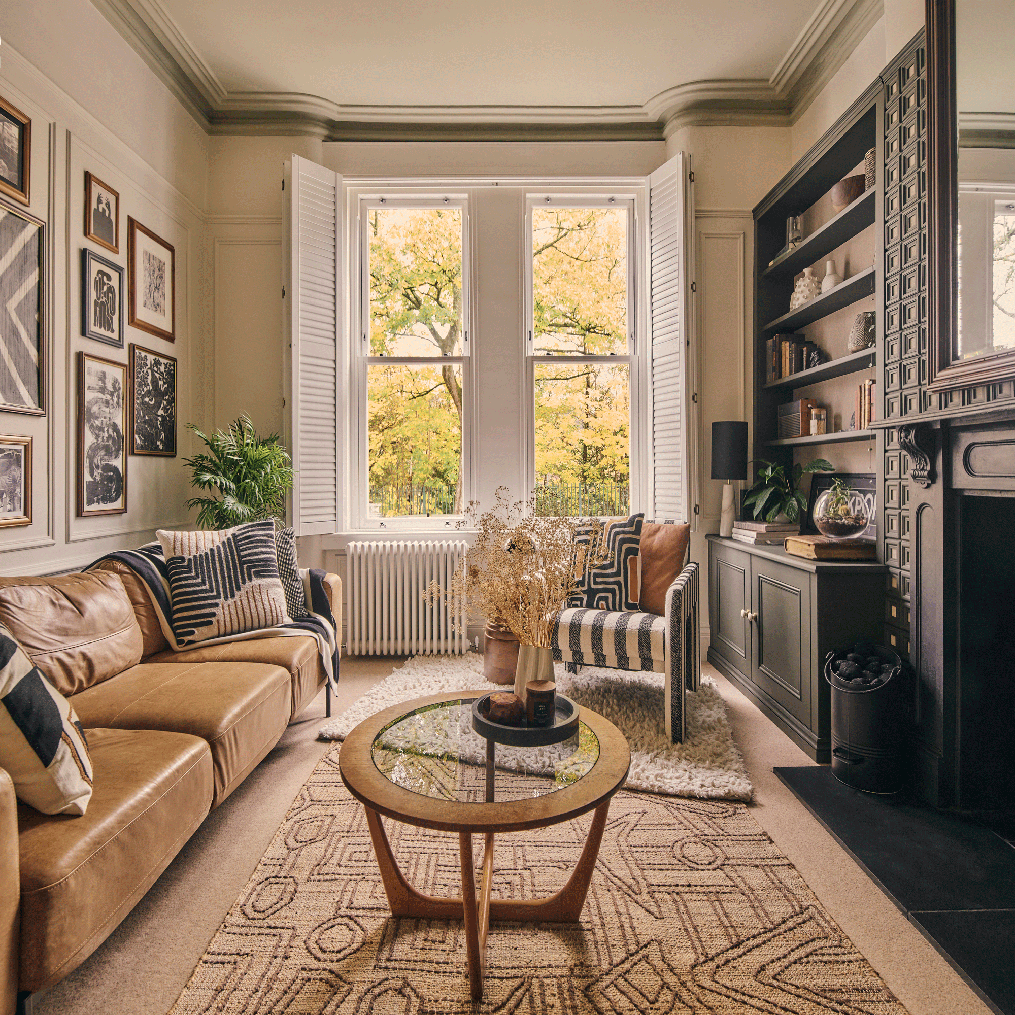 a living room with a brown leather sofa and gallery wall on one side and alcove shelving, fireplace with mantelpiece, black and white striped armchair and mid-century style coffee table