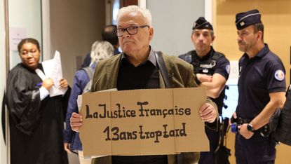 A man holds a placard saying ‘French justice, 13 years late’