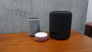En svart Amazon Echo Studio står på en träfärgad bänk bredvid två andra mindre smarthögtalare.