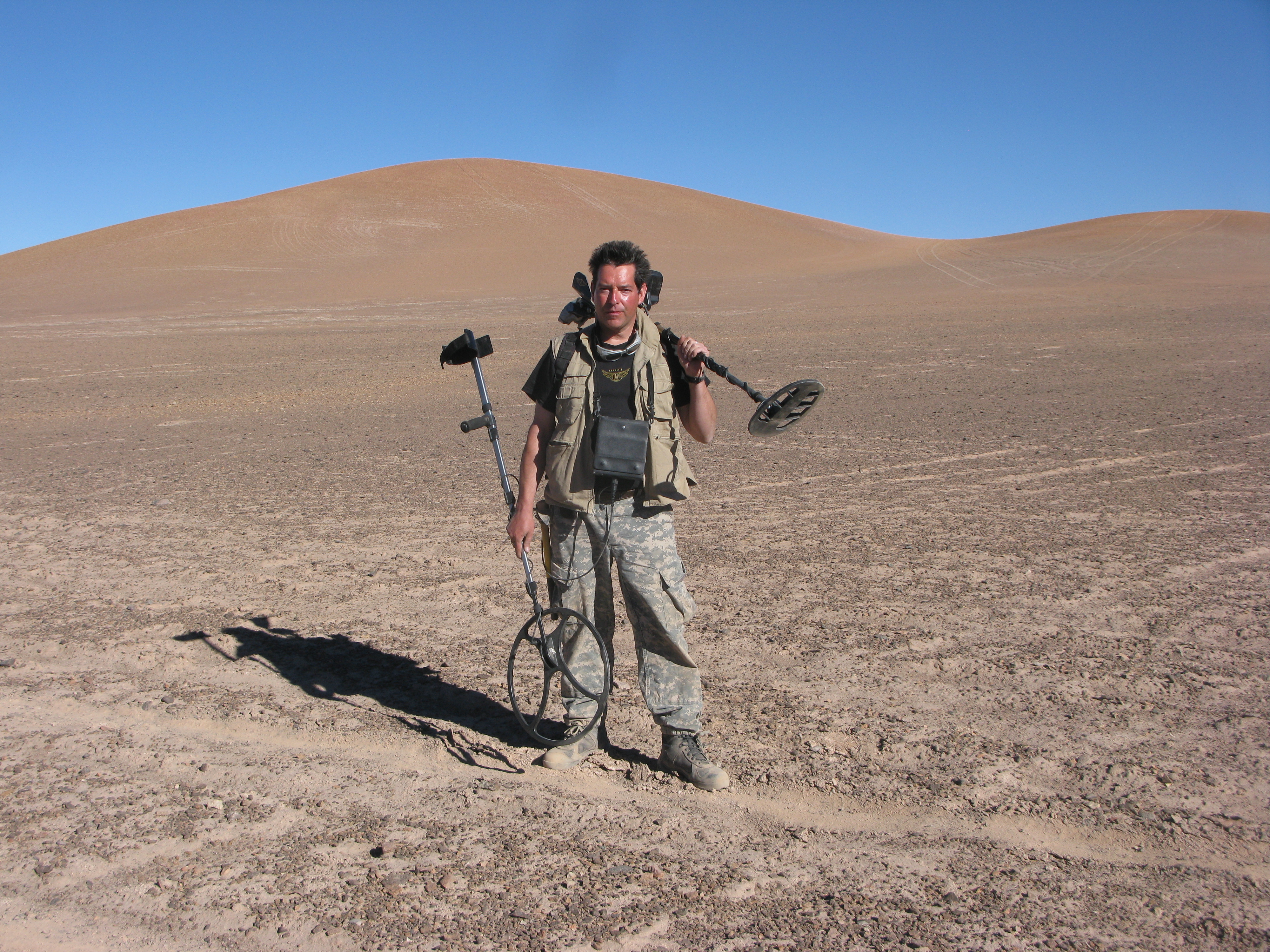 Un hombre en el desierto sosteniendo un detector de metales.
