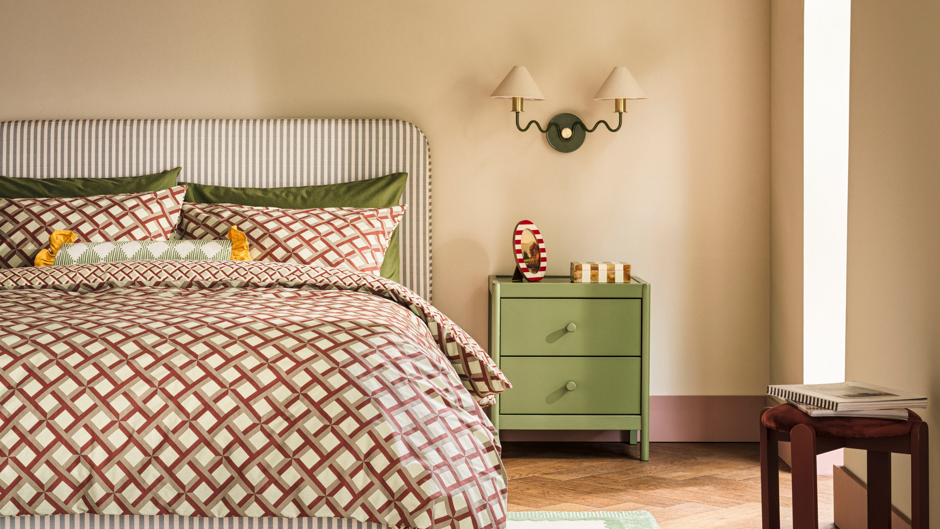 Double bed with geometric bedding, striped headboard, green bedside table, wood flooring, cream walls and green lights.