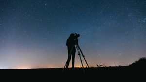 A person with a telescope silhouetted against the night sky