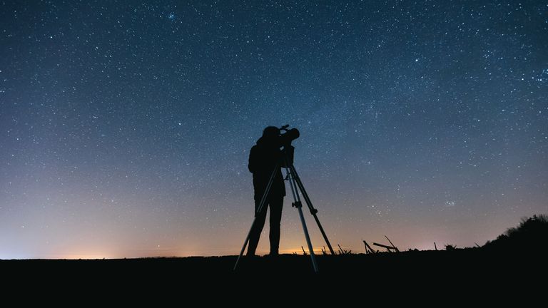 A person with a telescope silhouetted against the night sky