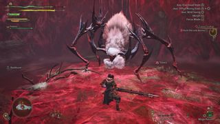 Monster Hunter Wilds review; A video game scene depicts a player character, dressed in dark attire, confronting a large, monstrous spider-like creature in a crimson-coloured environment.