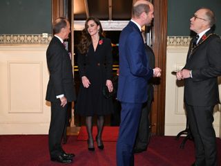 Kate Middleton wearing a black dress and Prince William wearing a blue suit and military medals greeting men during the Festival of Remembrance concert