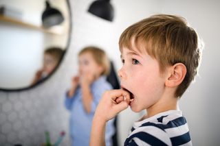 child standing in front of mirror with his fingers in his mouth, wiggling a loose tooth