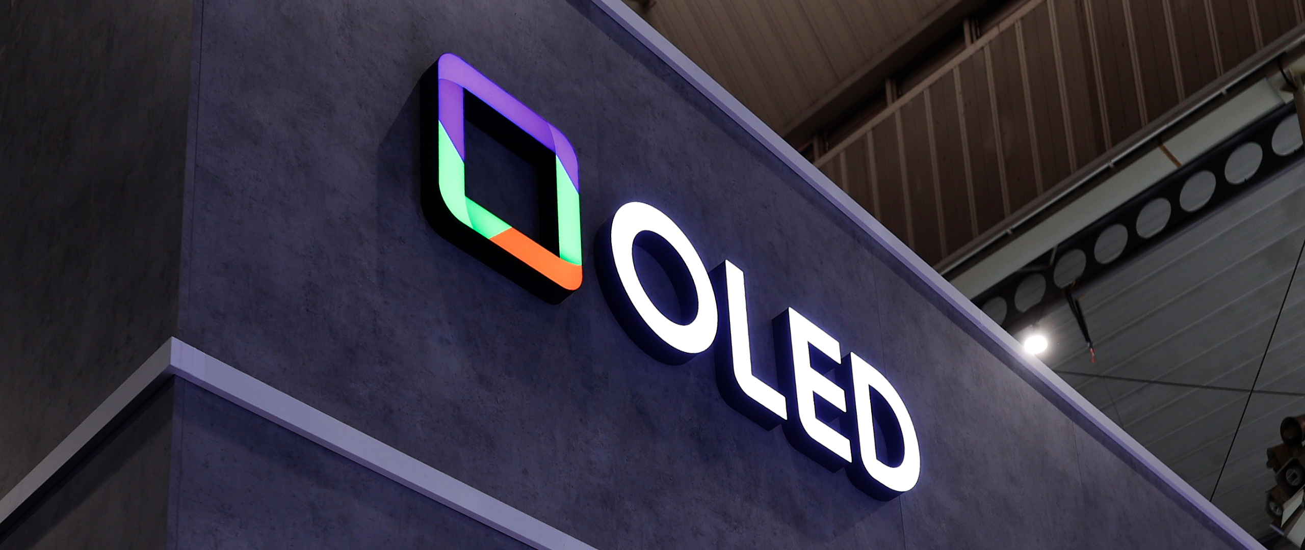 A sign at a trade-show with OLED in bold white letters with a colorful square next to it.