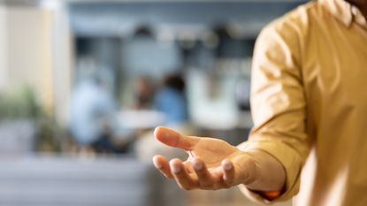 A man holds out his hand as if expecting someone to put something in it.