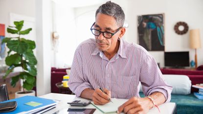 An older man sitting at a desk using a calculator and tablet