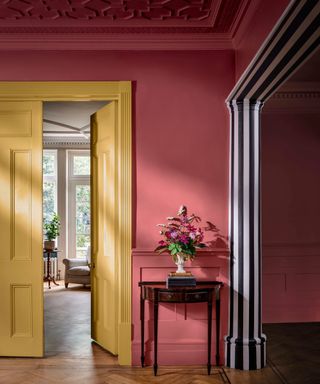 large hallway with dark pink walls, yellow double doors and dividing archway painted on the inside with black and white stripes