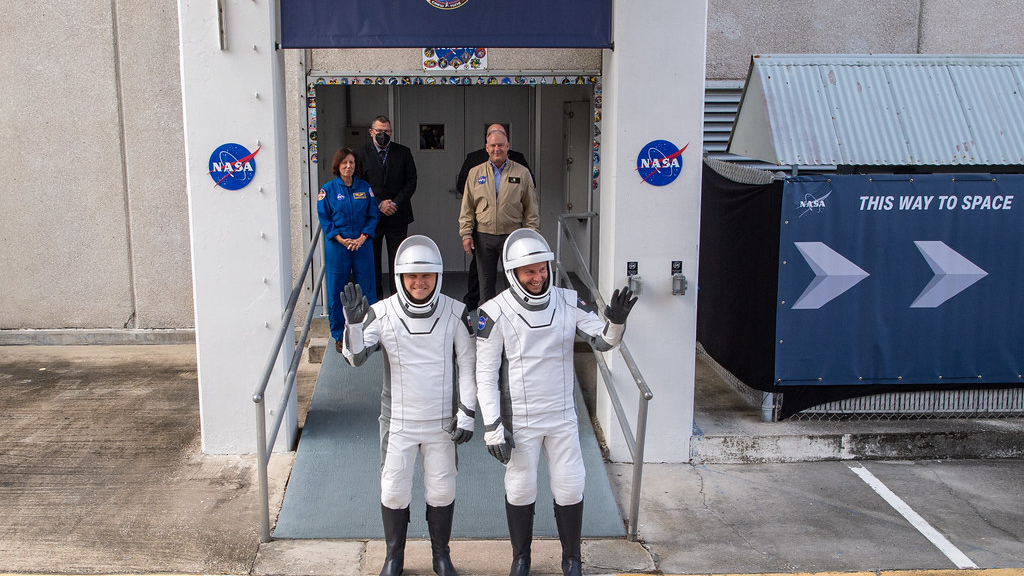 Astronot dari sembilan orang awak dengan pakaian antariksa putih dan hitam melambai saat mereka menuju landasan peluncuran.